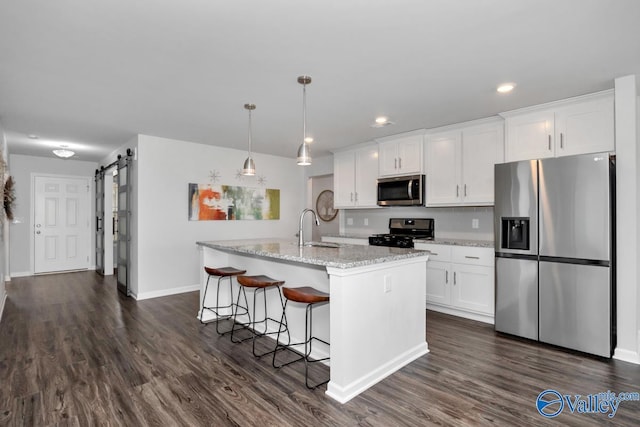 kitchen featuring a barn door, stainless steel appliances, white cabinetry, and a center island with sink