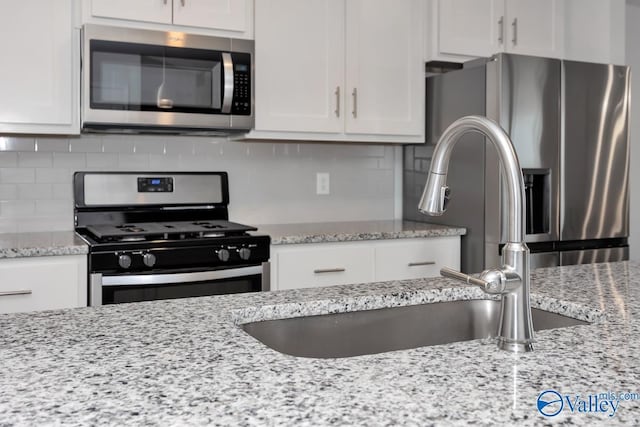 kitchen with light stone counters, white cabinetry, stainless steel appliances, and tasteful backsplash