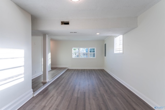 empty room with a textured ceiling, a healthy amount of sunlight, and dark hardwood / wood-style floors