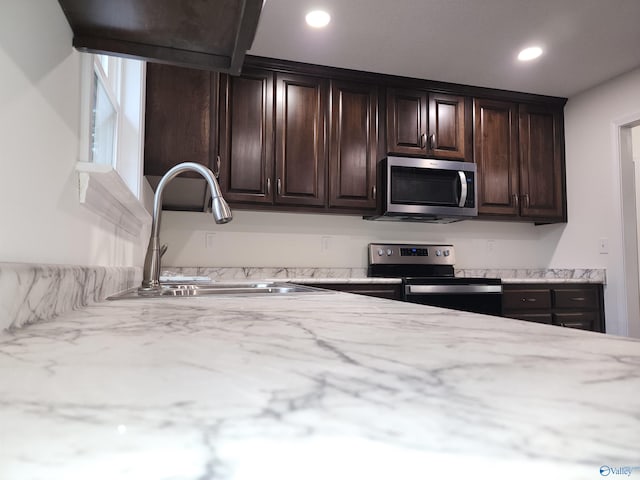 kitchen with dark brown cabinets, light stone countertops, appliances with stainless steel finishes, and sink