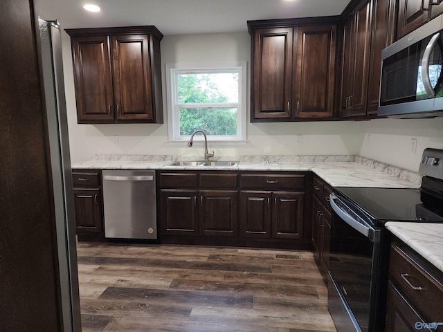 kitchen with light stone counters, dark hardwood / wood-style floors, stainless steel appliances, dark brown cabinetry, and sink