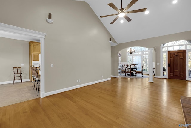 unfurnished living room with ceiling fan with notable chandelier, light hardwood / wood-style floors, and high vaulted ceiling