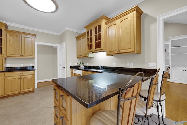 kitchen with a breakfast bar, sink, dark stone countertops, light tile patterned floors, and ornamental molding