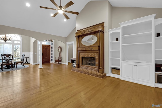 unfurnished living room with high vaulted ceiling, ceiling fan with notable chandelier, built in features, a fireplace, and light hardwood / wood-style floors