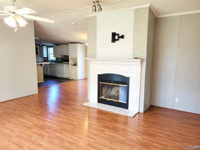 unfurnished living room with light wood-type flooring, ornamental molding, ceiling fan, sink, and a tiled fireplace