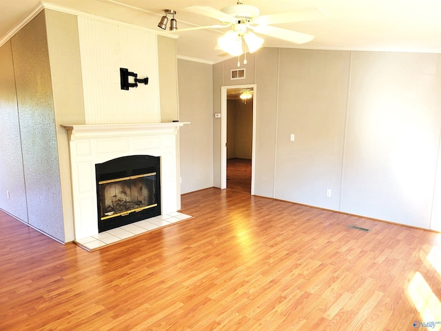 unfurnished living room featuring lofted ceiling, a tile fireplace, light hardwood / wood-style flooring, ceiling fan, and ornamental molding