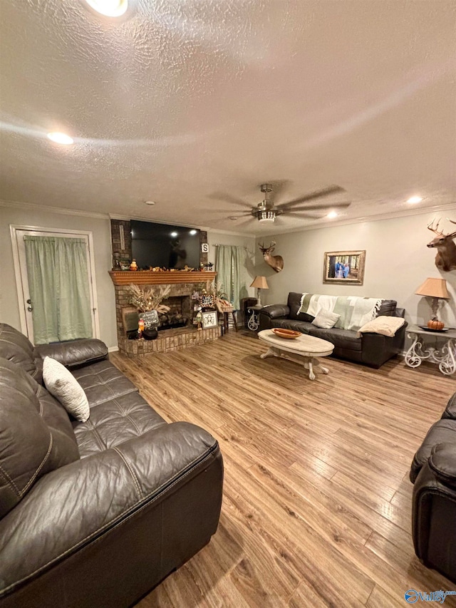 living room with a stone fireplace, ceiling fan, wood-type flooring, and a textured ceiling