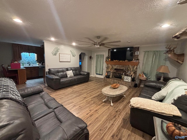 living room featuring ornamental molding, a textured ceiling, ceiling fan, hardwood / wood-style floors, and a stone fireplace