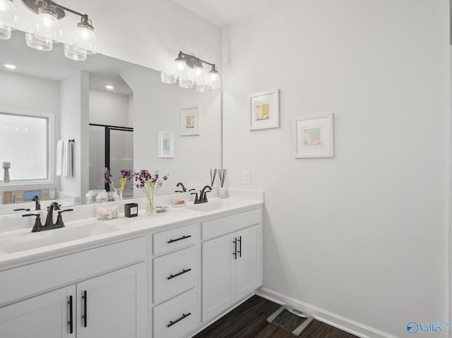 full bathroom featuring double vanity, a sink, a shower stall, and baseboards