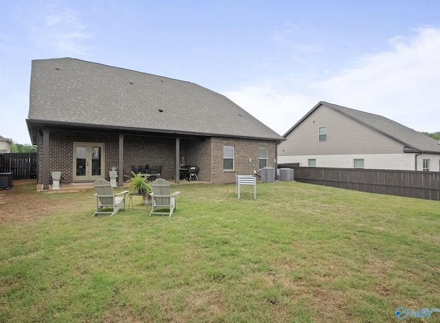 rear view of house featuring central AC unit, a yard, a fenced backyard, brick siding, and french doors