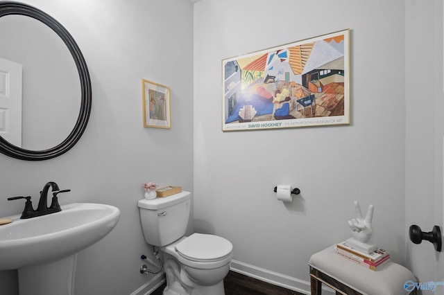 half bath featuring toilet, a sink, wood finished floors, and baseboards