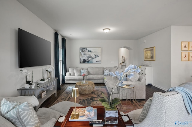 living room featuring arched walkways, dark wood-style flooring, and baseboards