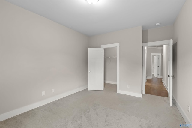 unfurnished bedroom featuring a walk in closet, light colored carpet, and a closet