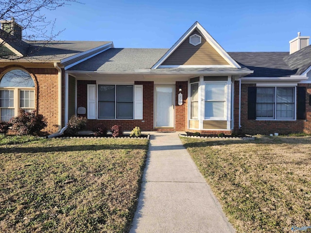 single story home featuring a shingled roof, a front lawn, brick siding, and a chimney