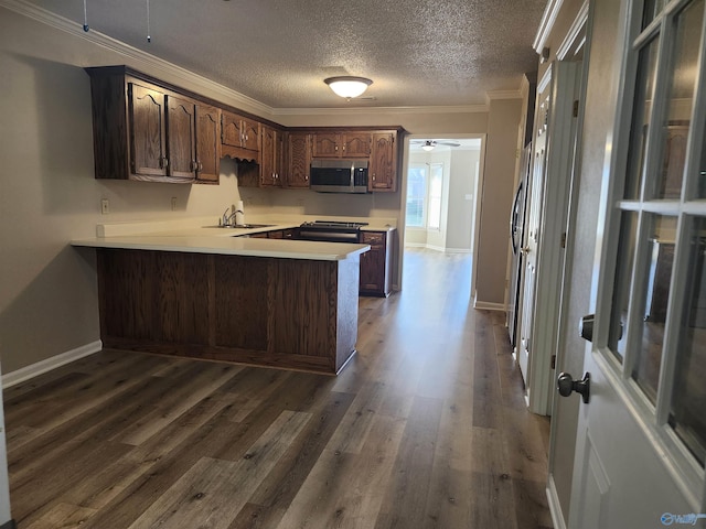 kitchen featuring stainless steel microwave, light countertops, a peninsula, dark wood-style floors, and a sink