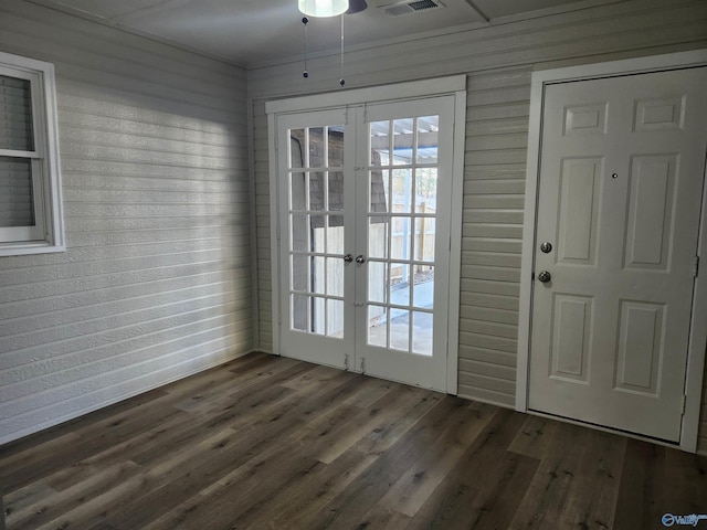 doorway with french doors, dark wood-type flooring, visible vents, and wooden walls