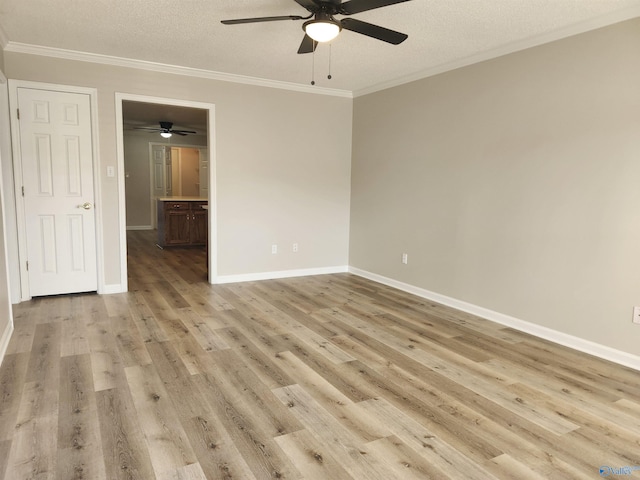 spare room featuring crown molding, baseboards, light wood-type flooring, and a textured ceiling