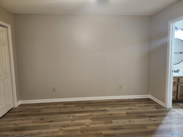 empty room with dark wood-style floors, a textured ceiling, and baseboards