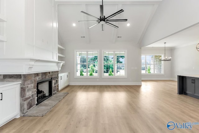 unfurnished living room featuring a stone fireplace, a chandelier, lofted ceiling with beams, and light hardwood / wood-style flooring