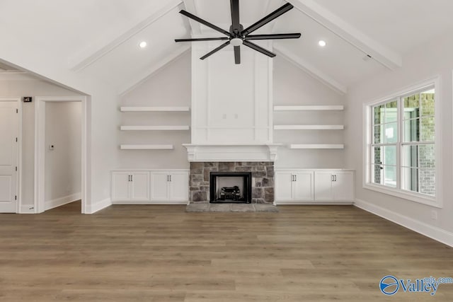 unfurnished living room featuring lofted ceiling with beams, a stone fireplace, hardwood / wood-style flooring, and ceiling fan