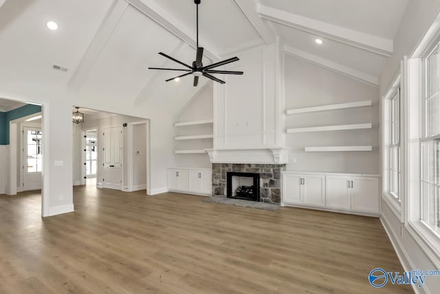 unfurnished living room with beam ceiling, wood-type flooring, high vaulted ceiling, ceiling fan, and a fireplace