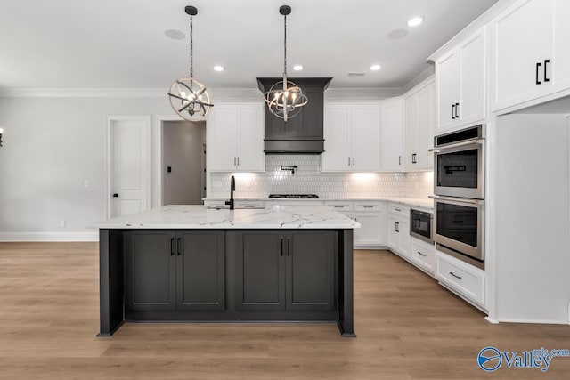 kitchen with double oven, an island with sink, white cabinets, light stone counters, and light wood-type flooring