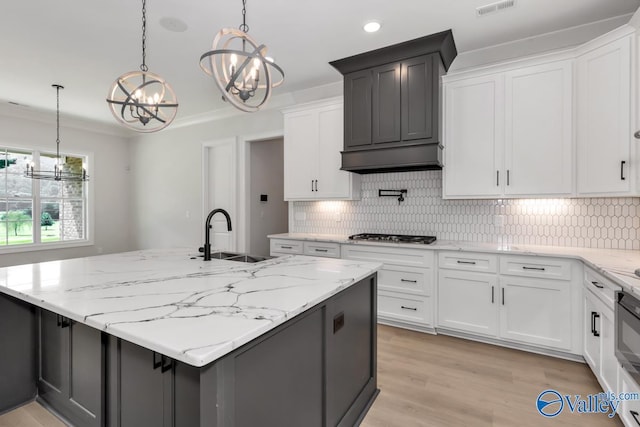 kitchen featuring decorative light fixtures, white cabinetry, an island with sink, sink, and an inviting chandelier