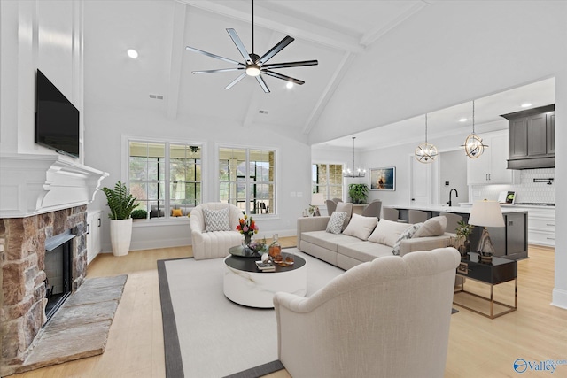 living room featuring a stone fireplace, high vaulted ceiling, a chandelier, beam ceiling, and light hardwood / wood-style flooring