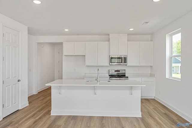 kitchen featuring stainless steel appliances, an island with sink, sink, and white cabinetry