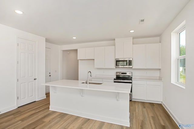 kitchen with stainless steel appliances, a kitchen island with sink, sink, and white cabinets