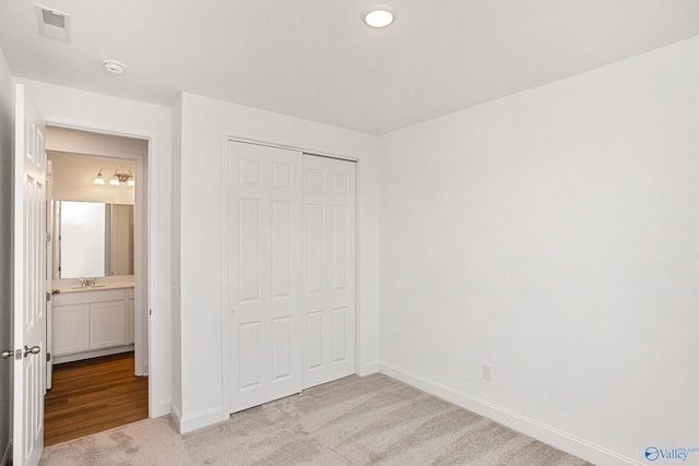 unfurnished bedroom with light colored carpet, ensuite bath, sink, and a closet