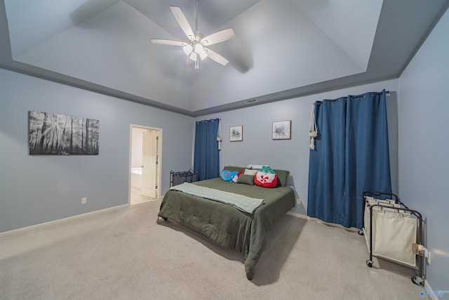 bedroom with ensuite bath, light colored carpet, vaulted ceiling, a tray ceiling, and ceiling fan