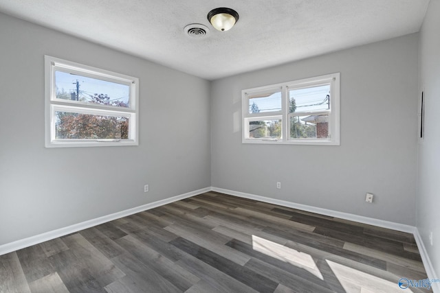 empty room with dark hardwood / wood-style flooring, a textured ceiling, and a wealth of natural light