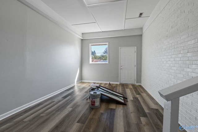 unfurnished room featuring brick wall and dark hardwood / wood-style flooring