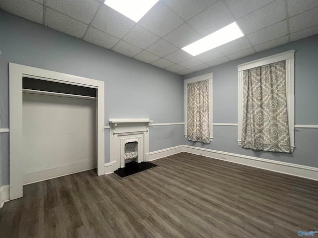 unfurnished living room featuring a paneled ceiling and dark hardwood / wood-style flooring