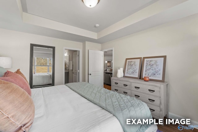 bedroom with baseboards, wood finished floors, a raised ceiling, and ensuite bath