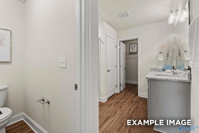 bathroom with toilet, baseboards, visible vents, and wood finished floors