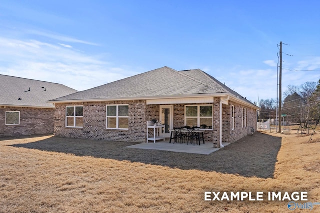 back of house with brick siding, roof with shingles, a patio area, and a yard