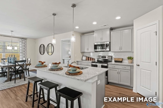 kitchen with a kitchen breakfast bar, backsplash, appliances with stainless steel finishes, wood finished floors, and a sink