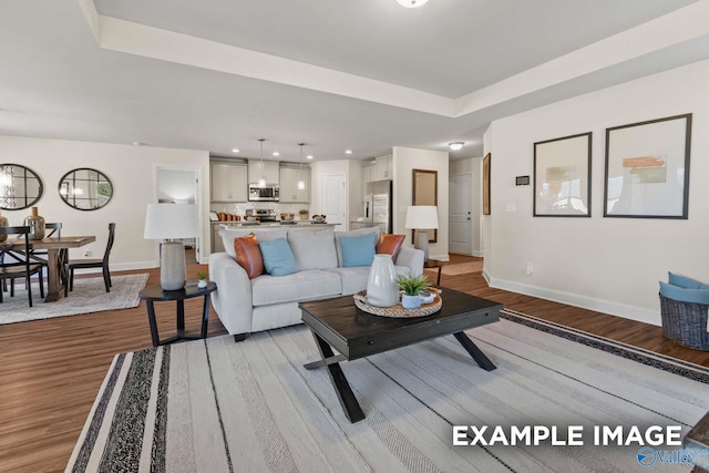 living room featuring baseboards, wood finished floors, and a tray ceiling