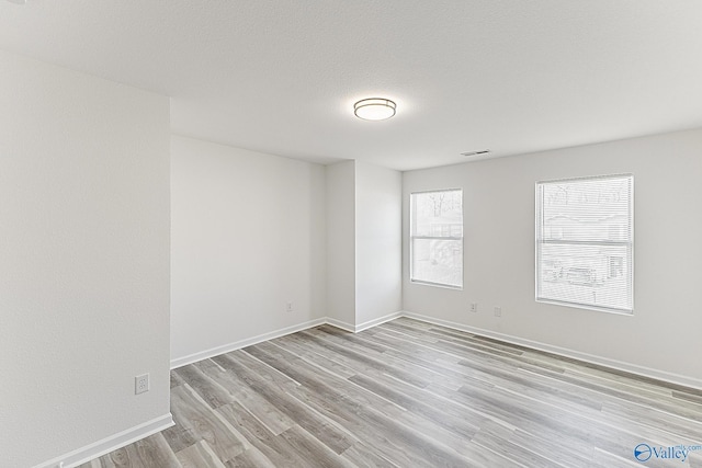 empty room with light wood-style floors, baseboards, visible vents, and a textured ceiling