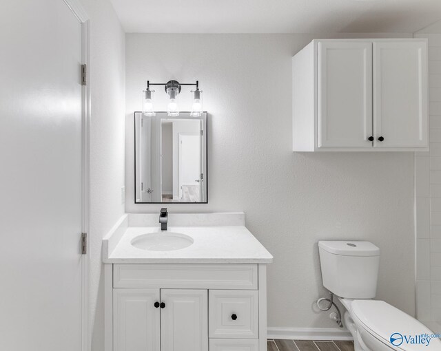 full bath with toilet, baseboards, wood finished floors, and vanity