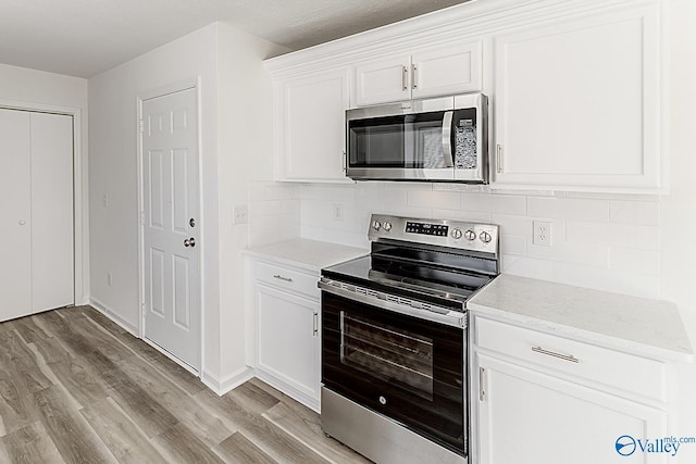 kitchen with stainless steel appliances, decorative backsplash, light wood-style floors, white cabinets, and light stone countertops