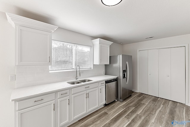 kitchen with appliances with stainless steel finishes, a sink, light wood-style floors, white cabinetry, and backsplash