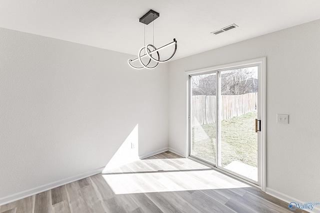 unfurnished dining area featuring baseboards, wood finished floors, visible vents, and a notable chandelier