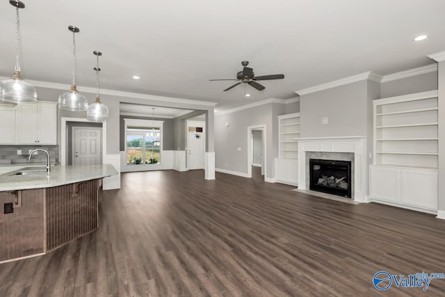 unfurnished living room featuring ornamental molding, built in features, sink, ceiling fan, and dark wood-type flooring