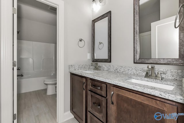 bathroom featuring double vanity, a sink, toilet, and shower / washtub combination