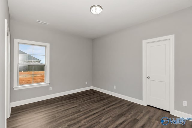 empty room with dark wood finished floors, baseboards, and visible vents