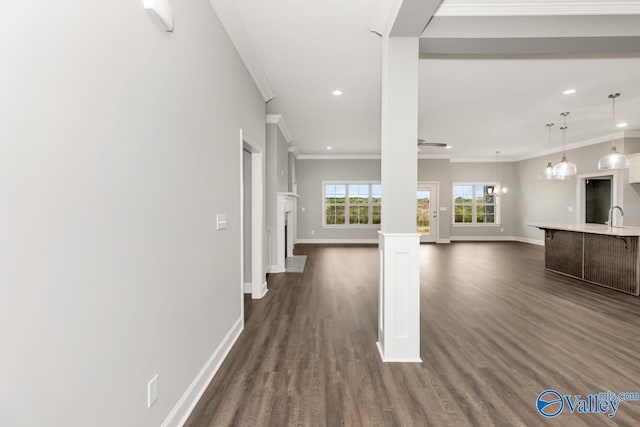 unfurnished living room featuring dark wood-type flooring, sink, an inviting chandelier, and ornamental molding