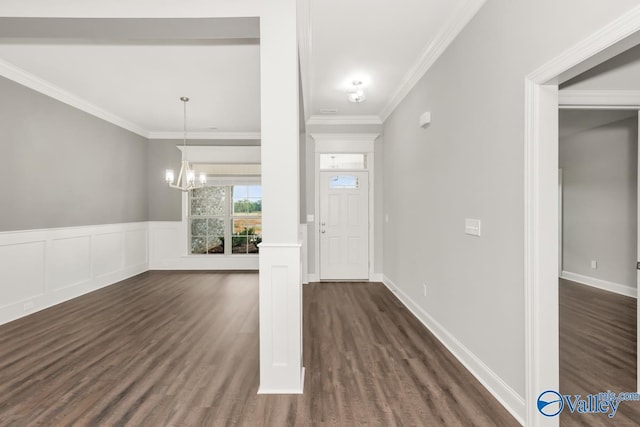 foyer with ornamental molding, a chandelier, dark wood finished floors, a decorative wall, and wainscoting